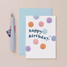 A cute birthday card with happy birthday lettering and smiley faces on a birthday card from the birthday card collection at Sister Paper Co.