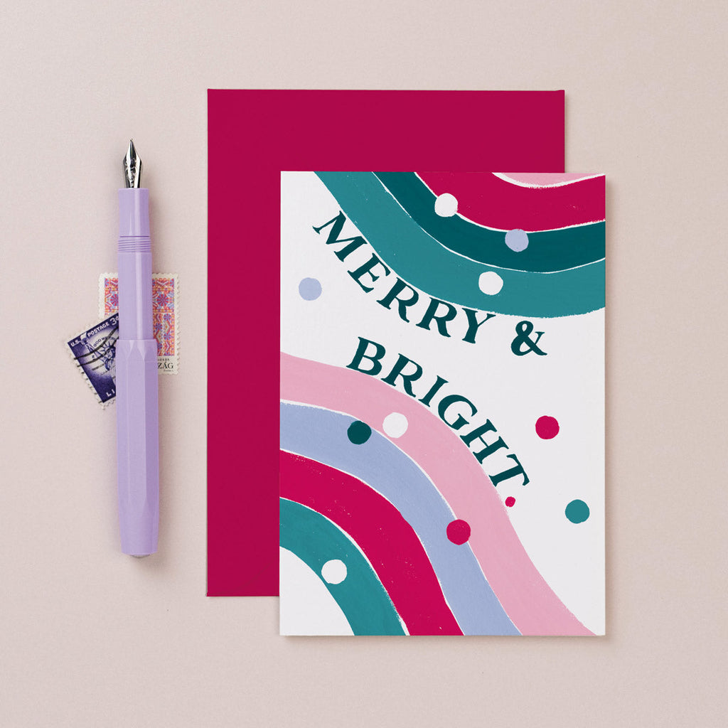 A rainbow with fun merry and bright lettering on a Christmas card from the colourful, rainbow Christmas card collection at Sister Paper Co.