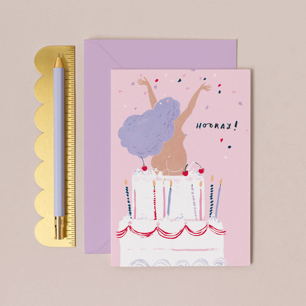 A girl jumping out of a giant cake on a rude funny womens birthday card from the female birthday card collection at Sister Paper Co.